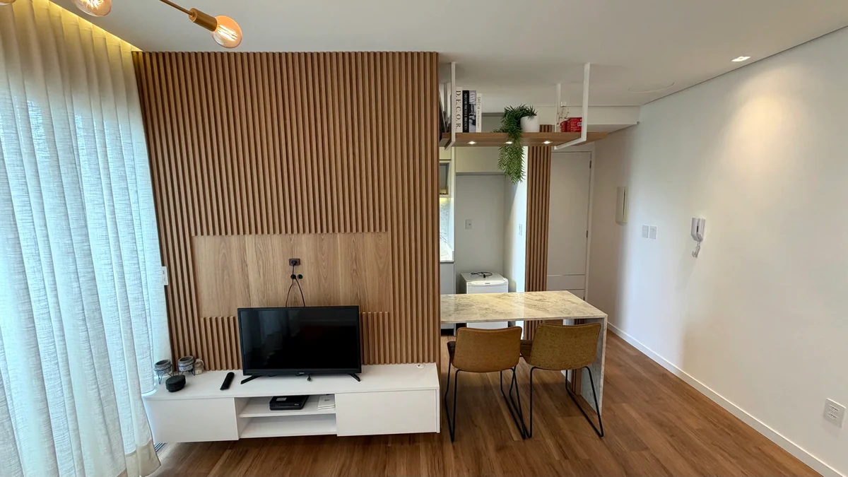 Sala do apartamento com painel ripado, rack e mesa.