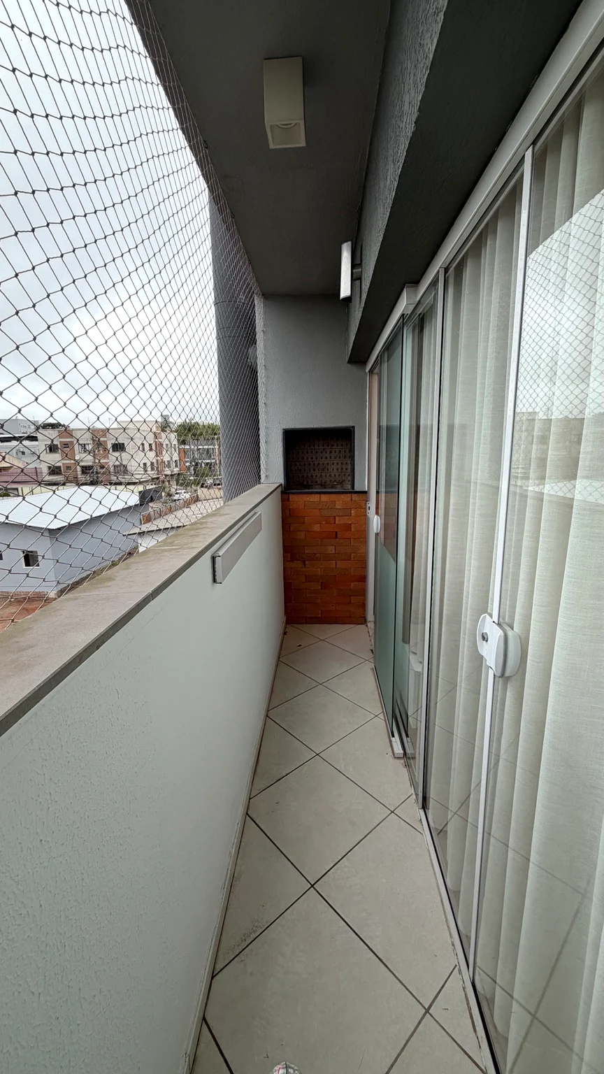 Sacada com rede de proteção, portas de vidro e churrasqueira ao fundo.